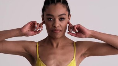 Hoşnutsuz bir kadın parmaklarıyla kulaklarını kapatıyor. Stüdyoda gri bir arka planda tek başına duruyor.