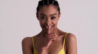 Stüdyoda gri bir arka planda duran seksi bir kadın gizli bir jest yapıyor.