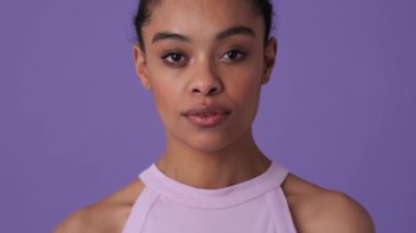 Gündelik giysiler giyen mutlu genç bir kadın stüdyodaki menekşe arkaplan üzerinde gizli bir jest yapıyor.