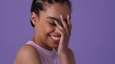 Sıradan kıyafetler giyen utangaç genç bir kadın, stüdyodaki menekşe arkaplanının başında tek başına kameraya bakıyor.