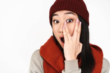 Asyalı şok olmuş güzel bir kız şaşkınlığını dile getiriyor ve yüzünü beyaz arka planda gizliyor.