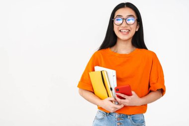 Asyalı mutlu öğrenci elinde akıllı telefon ve beyaz arka planda izole edilmiş egzersiz kitapları tutuyor.
