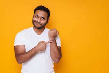 Asyalı, hayal kırıklığına uğramış genç bir adam, sarı arka planda izole bir şekilde koluna el sallıyor.