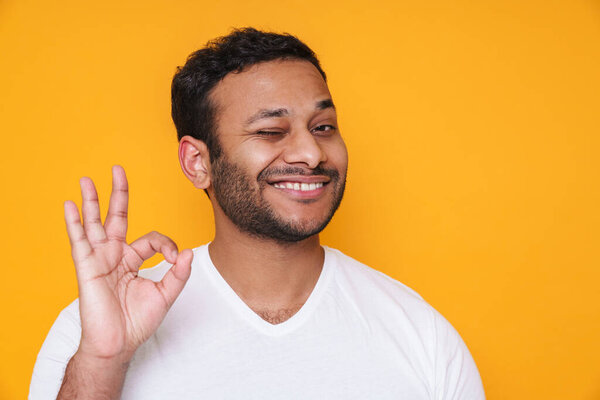 Азиатский молодой небритый мужчина улыбается и жестикулирует хорошо знак изолирован на желтом фоне