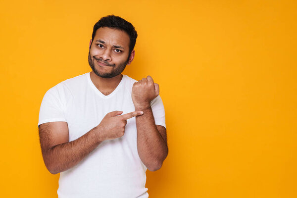 Азиатский молодой разочарованный мужчина жестом на руку, как поздно время изолированы на желтом фоне