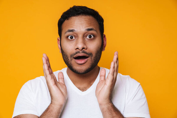 Азиатская брюнетка небритый удивленный мужчина поднимает руки к его лицу изолированы на желтом фоне