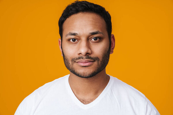 Азиатский уверенный в себе небритый мужчина позирует и смотрит в камеру изолированы на желтом фоне