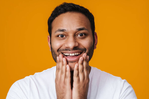 Азиатский счастливый небритый мужчина улыбается и касается подбородка изолированы на желтом фоне