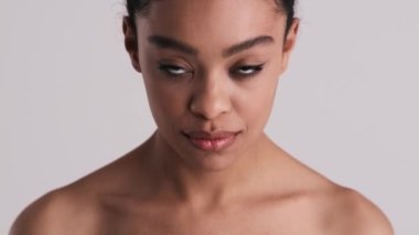 Mutlu, yarı çıplak bir kadının yakın plan görüntüsü kameraya bakıyor ve stüdyonun gri arka planında tek başına gülüyor.