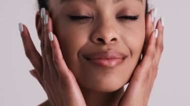 Mutlu, yarı çıplak bir kadının yakın plan görüntüsü stüdyonun gri arka planında tek başına duran tenine dokunuyor.