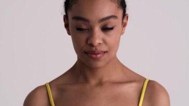 Mutlu bir Amerikalı kadın kameraya gülümsüyor. Stüdyonun gri arka planında tek başına duruyor.