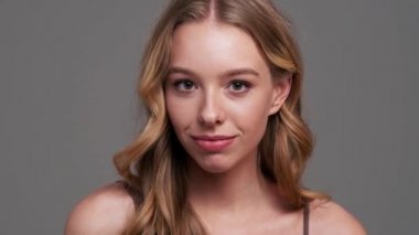 Güzel bir genç bayan, stüdyodaki gri arka planda tek başına duran kameraya hava öpücüğü gönderiyor.