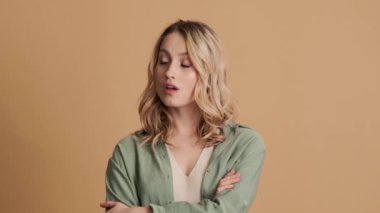 Kendinden emin genç bir kadın parmağını sallıyor. Stüdyoda bej arka planda tek başına duruyor.