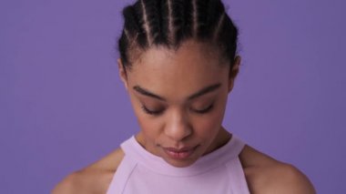 Gündelik giysiler giyen mutlu bir Afrikalı genç kadın gözlerini açıyor ve stüdyoda Violet 'in arka planında yalnız başına kameraya bakıyor.