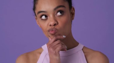 Sıradan kıyafetler giyen gülümseyen genç bir kadın, stüdyoda menekşe arkaplan üzerinde parmağını kaldırırken bir fikir üretiyor.