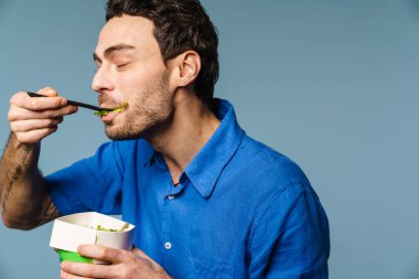 Mavi arka planda salata yerken gülümseyen yakışıklı adam.