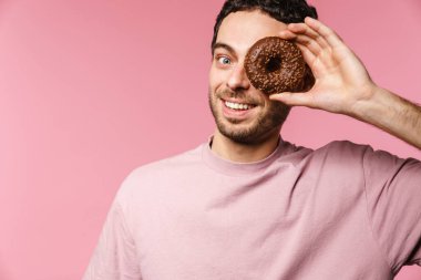 Pembe arka planda izole edilmiş donutla eğlenirken gülümseyen yakışıklı adam.