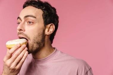 Pembe arka planda izole bir şekilde kamerada çörek yiyen mutlu ve aç bir adam.