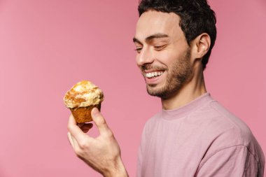 Pembe arka planda izole edilmiş kek ile poz verirken gülen neşeli yakışıklı adam.