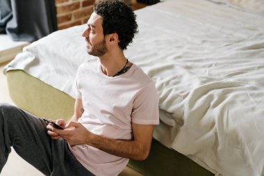 Yakışıklı, tıraşsız, neşeli adam. Yatak odasında yerde otururken cep telefonunda daktilo yazıyor.