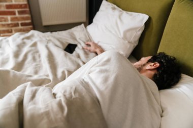 Yatakta yatarken cep telefonuyla uyuyan huzurlu bir adam.