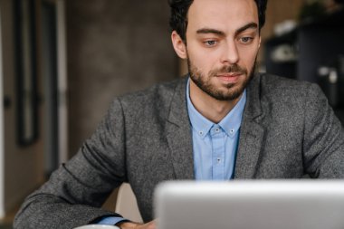 Evde çalışırken laptop kullanan yakışıklı bir iş adamı.