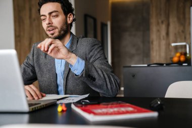 Evde dizüstü bilgisayarla çalışırken el kol hareketi yapan yakışıklı bir iş adamı.