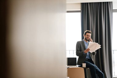 Kapalı alanda belgeleri incelerken cep telefonuyla konuşan yakışıklı bir işadamı.