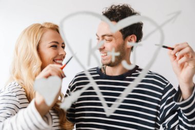 Güzel, gülümseyen, birbirine aşık genç bir çift, beyaz arka planda soyutlanmış valantines günlerinde baş harfleriyle bir kalp sembolü çiziyor.