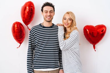 Sevgililer Günü 'nü beyaz arka planda izole edilmiş kırmızı kalp şeklinde balonlarla kutlayan çekici genç çift.