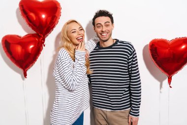 Sevgililer Günü 'nü beyaz arka planda izole edilmiş kırmızı kalp şeklinde balonlarla kutlayan çekici genç çift.