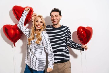 Sevgililer Günü 'nü beyaz arka planda izole edilmiş kırmızı kalp şeklinde balonlarla kutlayan çekici genç çift.