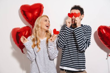 Sevgililer Günü 'nü beyaz arka planda izole edilmiş kırmızı kalp şeklinde balonlarla kutlayan çekici genç çift.