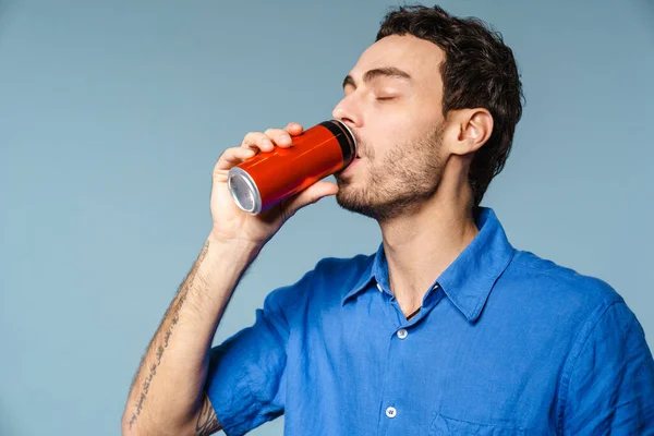 Happy handsome guy drinking soda with eyes closed isolated over blue background