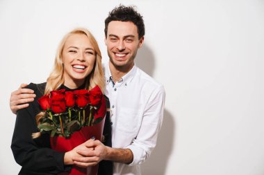 Romantik, genç ve mutlu bir çift birlikte bir olayı kutluyor. Beyaz arka planda izole edilmiş kırmızı gül buketi tutan kadın.