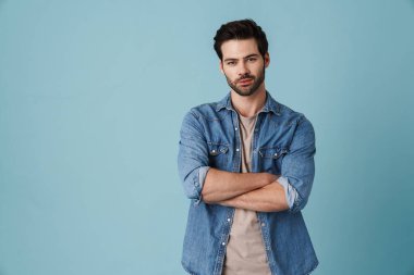 Mavi arka planda elleri çapraz duran genç ve yakışıklı bir adam.