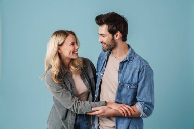 Genç, güzel, beyaz bir erkek ve kadın mavi arka planda izole edilmiş kameraya gülümseyip sarılıyorlar.