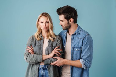 Yakışıklı esmer adam, mutsuz kıza sarılıyor ve konuşuyor. Mavi arka planda izole edilmiş.