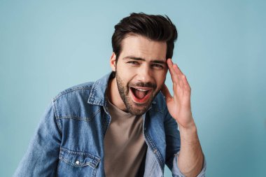 Genç, yakışıklı, heyecanlı adam mavi arka planda mahsur kalmış kamerada şaşkınlığını ifade ediyor.