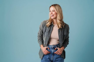 Mutlu güzel sarışın kız gülümsüyor ve mavi arka planda bir kenara bakıyor.