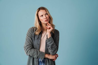 Mutlu, güzel, şaşkın, düşünceli, mavi arka planda bir kenara bakan kız.