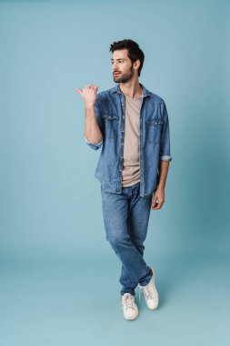 Genç yakışıklı adam mavi arka planda izole edilmiş boşluğu işaret ediyor.