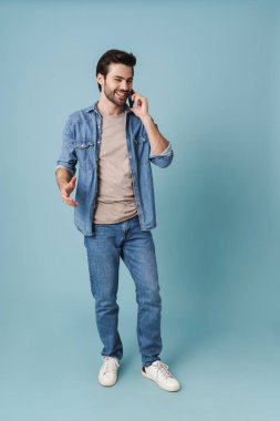 Genç, yakışıklı, beyaz adam mavi arka planda cep telefonuyla konuşuyor.