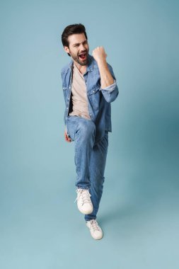 Genç, yakışıklı, tıraşsız, çığlık atan ve işaret eden adam mavi arka planda izole edilmiş.