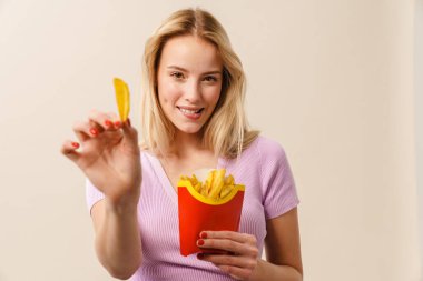 Beyaz arka planda izole edilmiş kameraya patates kızartması gösterirken gülümseyen güzel kız.