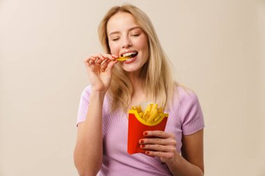 Neşeli güzel kız gülerken beyaz arka planda izole edilmiş patates kızartması yiyor.