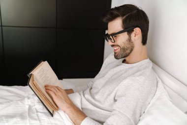 Mutlu genç adam evde dinlenirken gülümsüyor ve kitap okuyor.