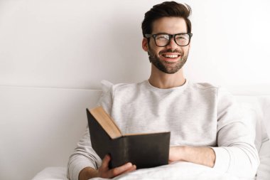 Mutlu genç adam evde dinlenirken gülümsüyor ve kitap okuyor.