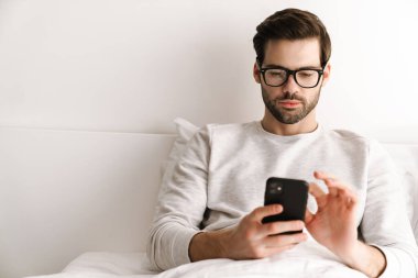 Evde dinlenirken cep telefonu kullanan gözlüklü ciddi bir genç adam.