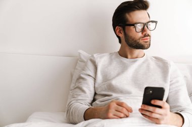 Evde dinlenirken cep telefonu kullanan gözlüklü ciddi bir genç adam.